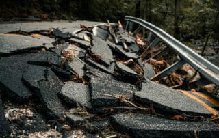 Rubble from a collapsed road with a twisted guardrail in the background