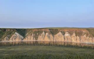 Slate brown bluffs overlooking the Porcupine River with large green pines in the foreground